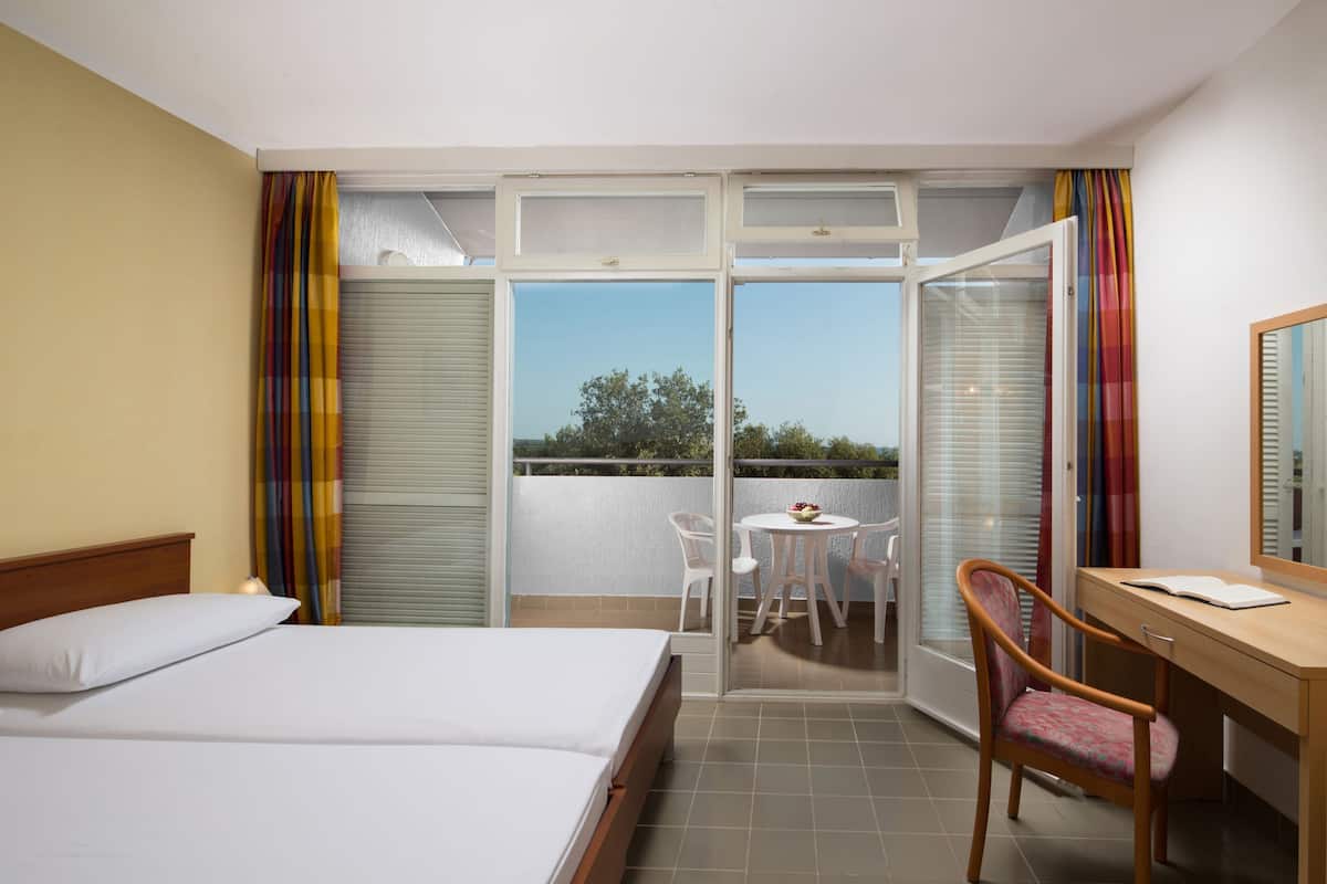 A hotel room with a bed, a desk, a chair, a small table, and a balcony with a view.