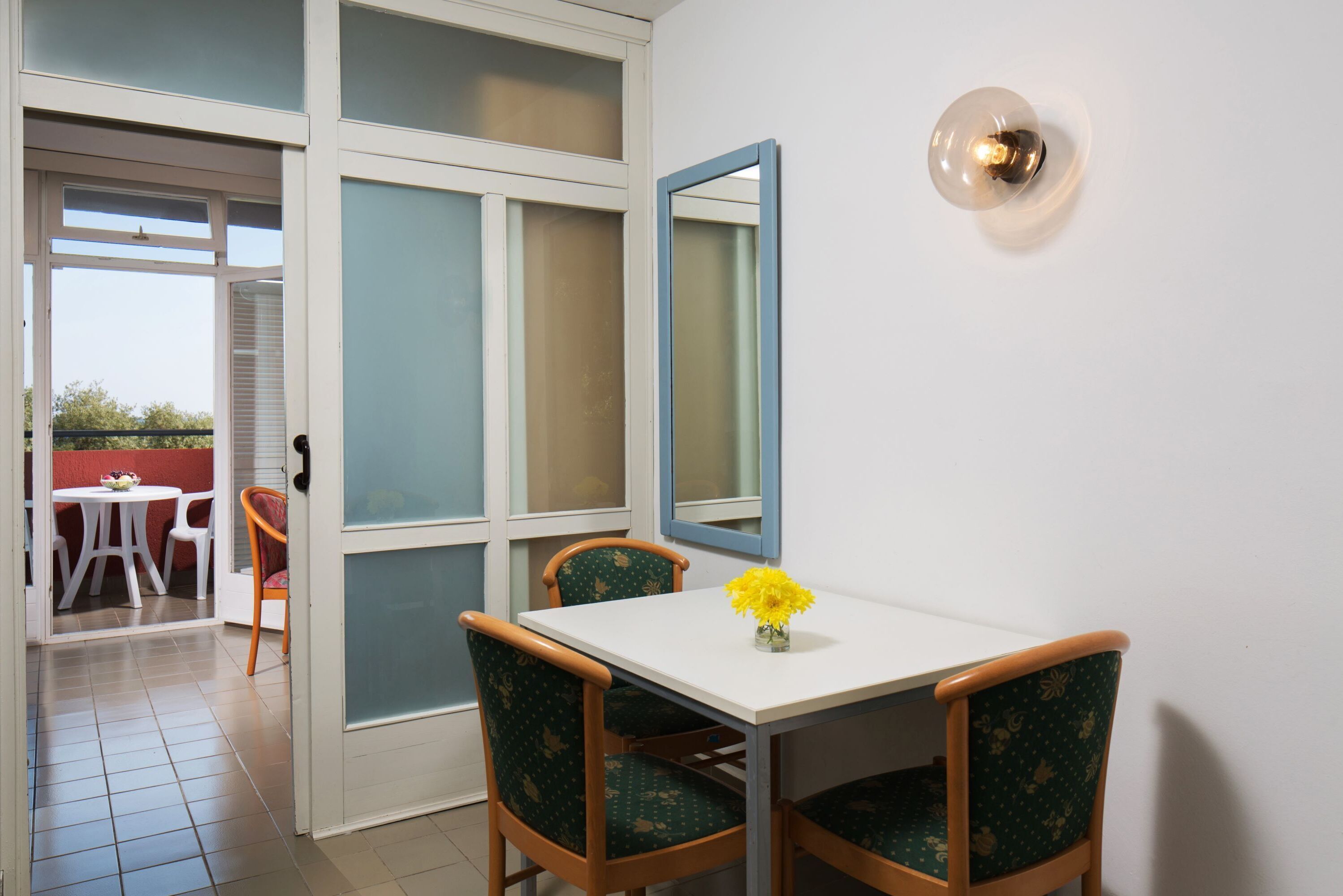 A dining area with a white table, green upholstered chairs, and a yellow flower vase.