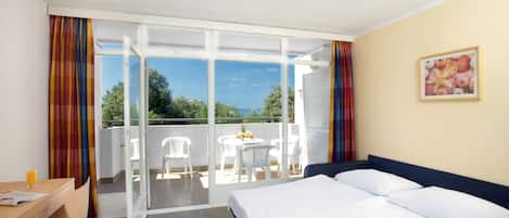 A hotel room with a bed, a desk with a chair, a table with chairs, and a balcony with a table and chairs.