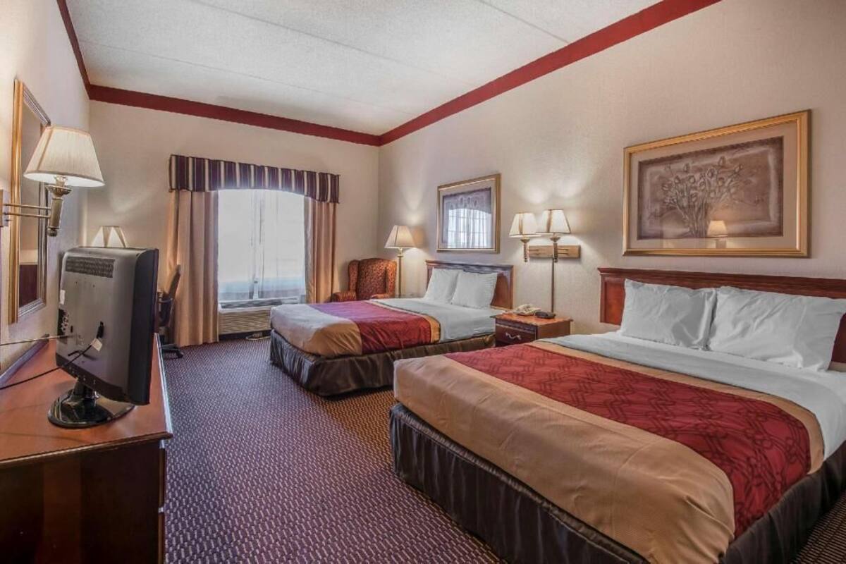 A hotel room with two beds, a television, a desk, and a window with curtains.