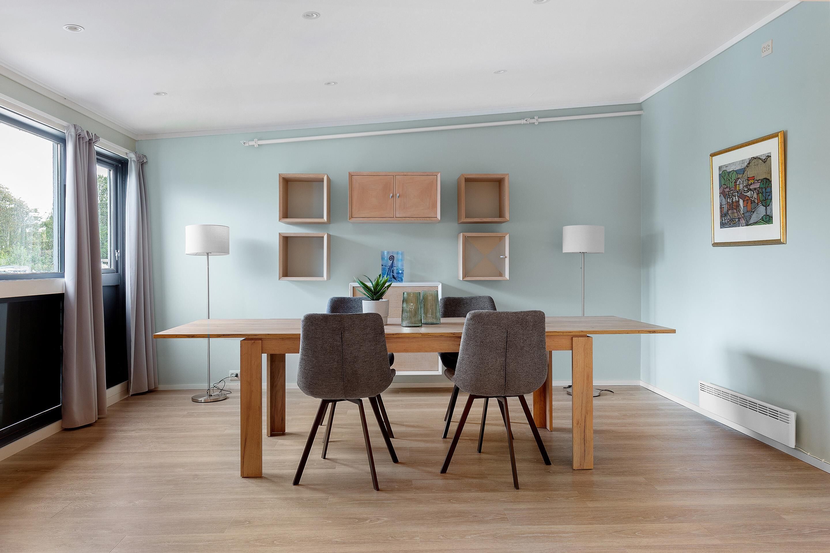 A modern dining area with a wooden table and two grey chairs, a potted plant, and a framed picture on the wall.