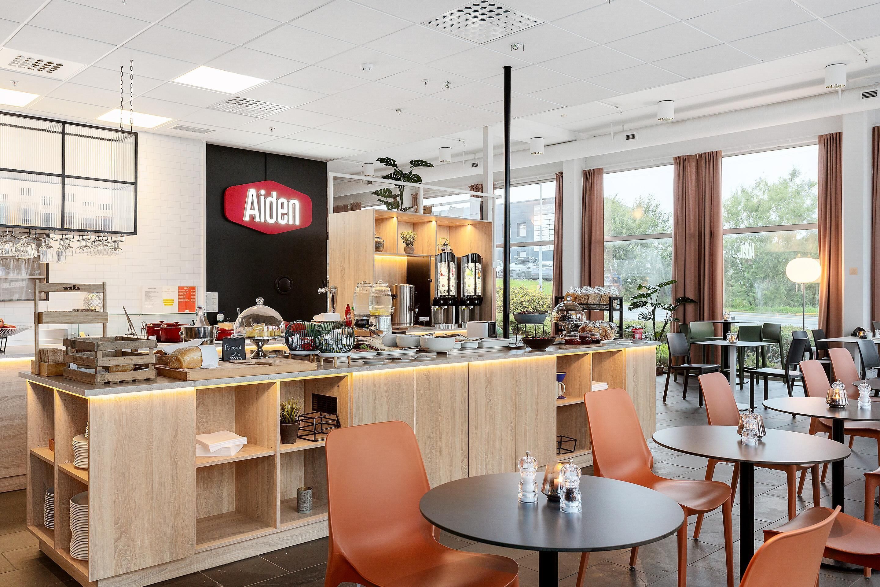 Un café moderne avec un comptoir en bois, des chaises orange et une vue sur la verdure environnante.