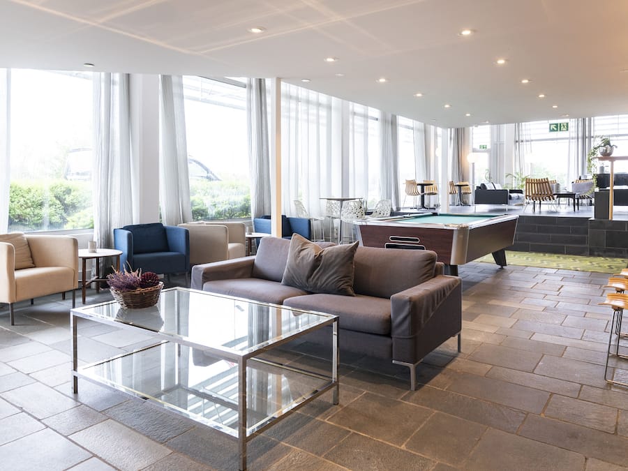 Un salón moderno con mesa de billar, asientos cómodos y ventanas amplias con vistas al exterior.