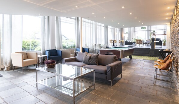 Un salón moderno con mesa de billar, asientos cómodos y ventanas amplias con vistas al exterior.