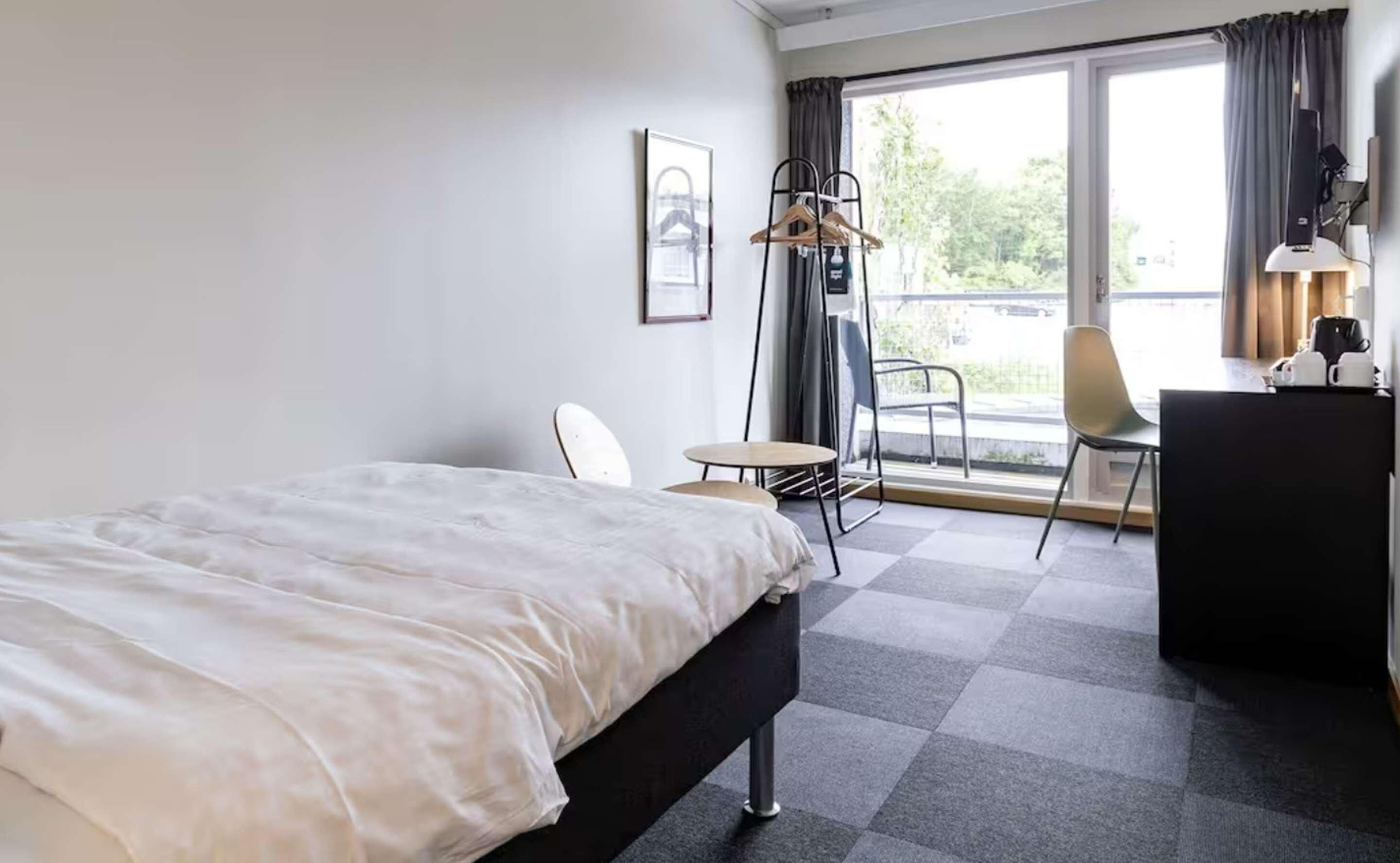 Een hotelkamer met een bed, een bureau, een stoel, een klein tafeltje en uitzicht op de omgeving.