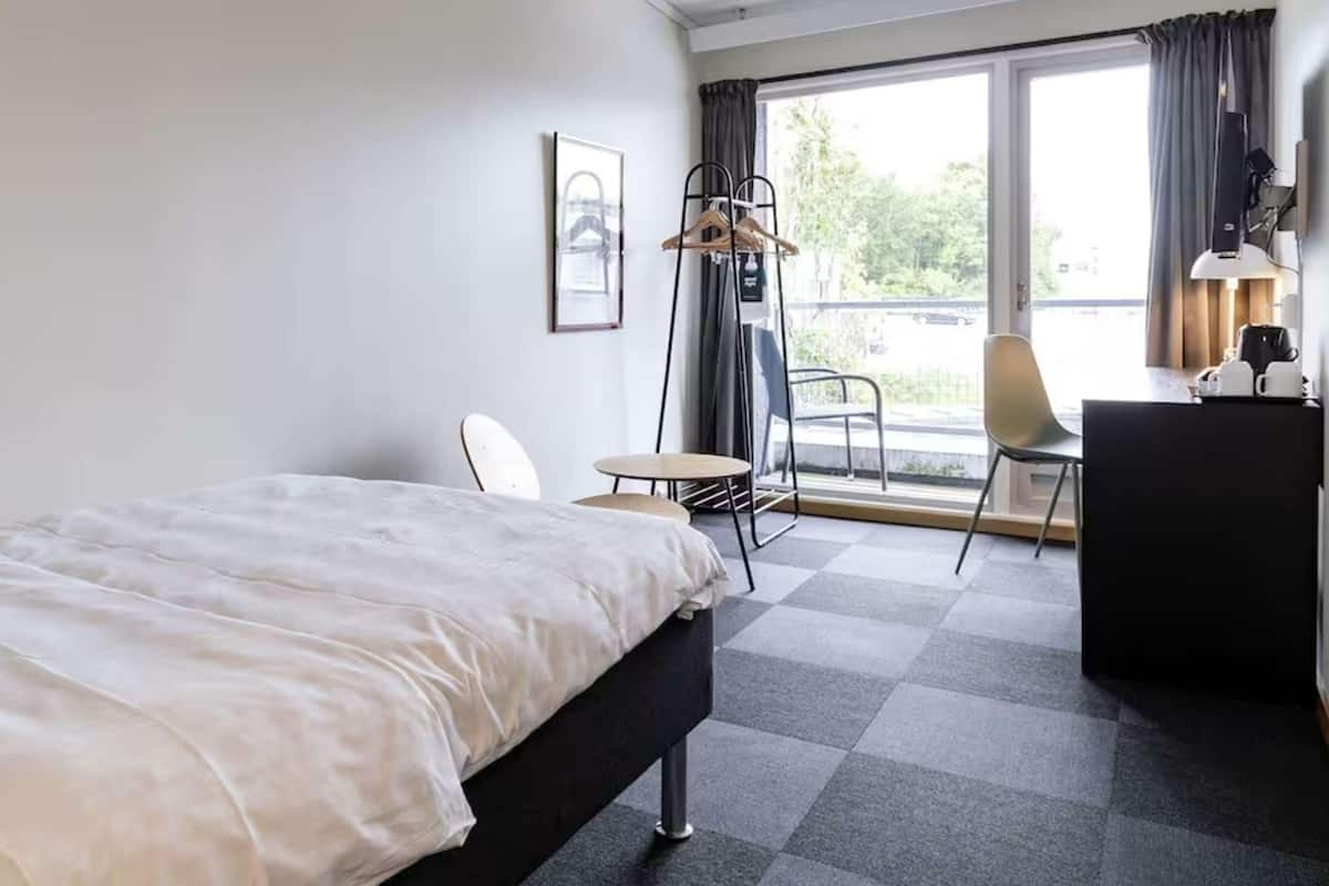 Habitación de hotel con cama, escritorio, silla, una mesita y vistas al exterior.