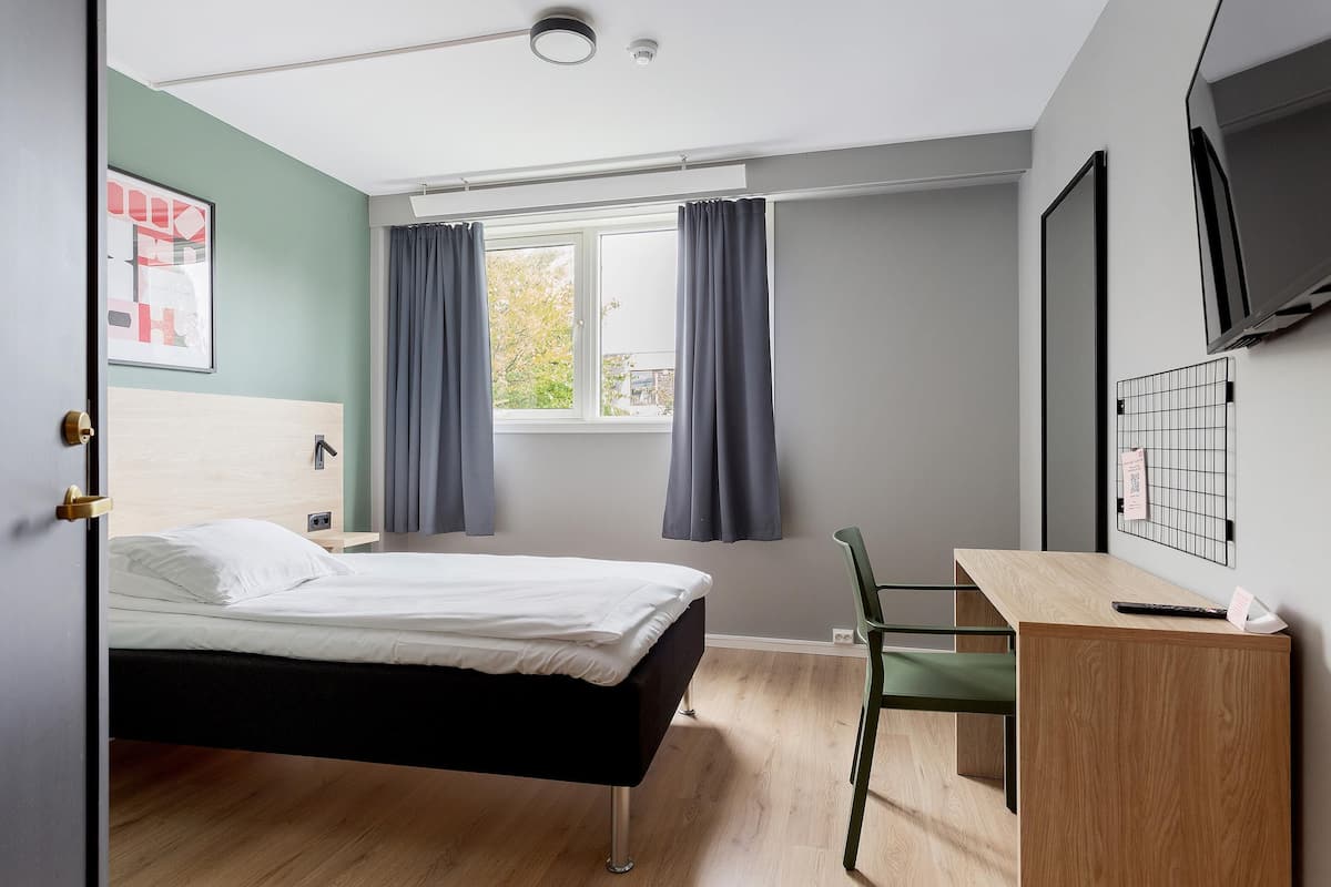 Un dormitorio moderno con cama, escritorio, silla y televisor montado en la pared.