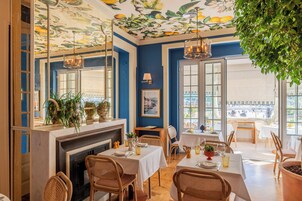 A dining area with tables set for two, a fireplace, and a view of the outside.