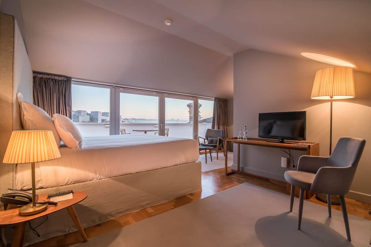 Una habitación de hotel moderna con una cama grande, un escritorio con televisor, una silla y una lámpara.