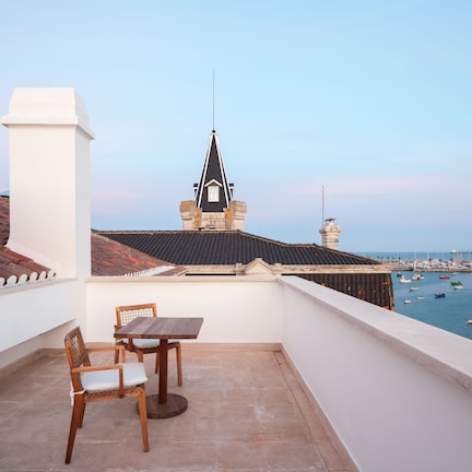 A balcony with a table and chairs, overlooking a marina with boats and a distant view of a building with a pointed roof.