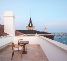 A balcony with a table and chairs, overlooking a marina with boats and a distant view of a building with a pointed roof.