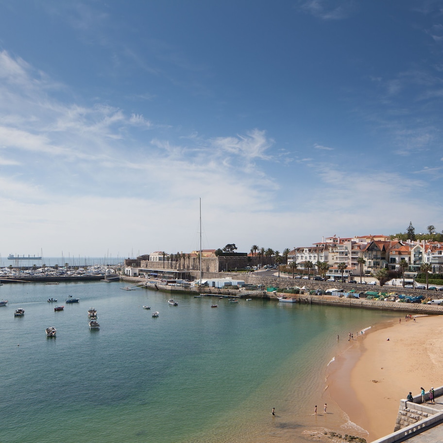 A coastal town with a sandy beach, boats in the water, and buildings along the shore.