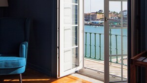 Una habitación con un amplio ventanal corredera que da a un balcón con vistas al mar y edificios.