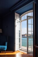 A room with a large sliding glass door leading to a balcony with a view of the sea and buildings.