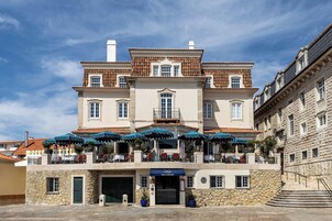 Un edificio de dos plantas con fachada de piedra, un balcón con sombrillas y un letrero que dice "VILLA CASCAIS".