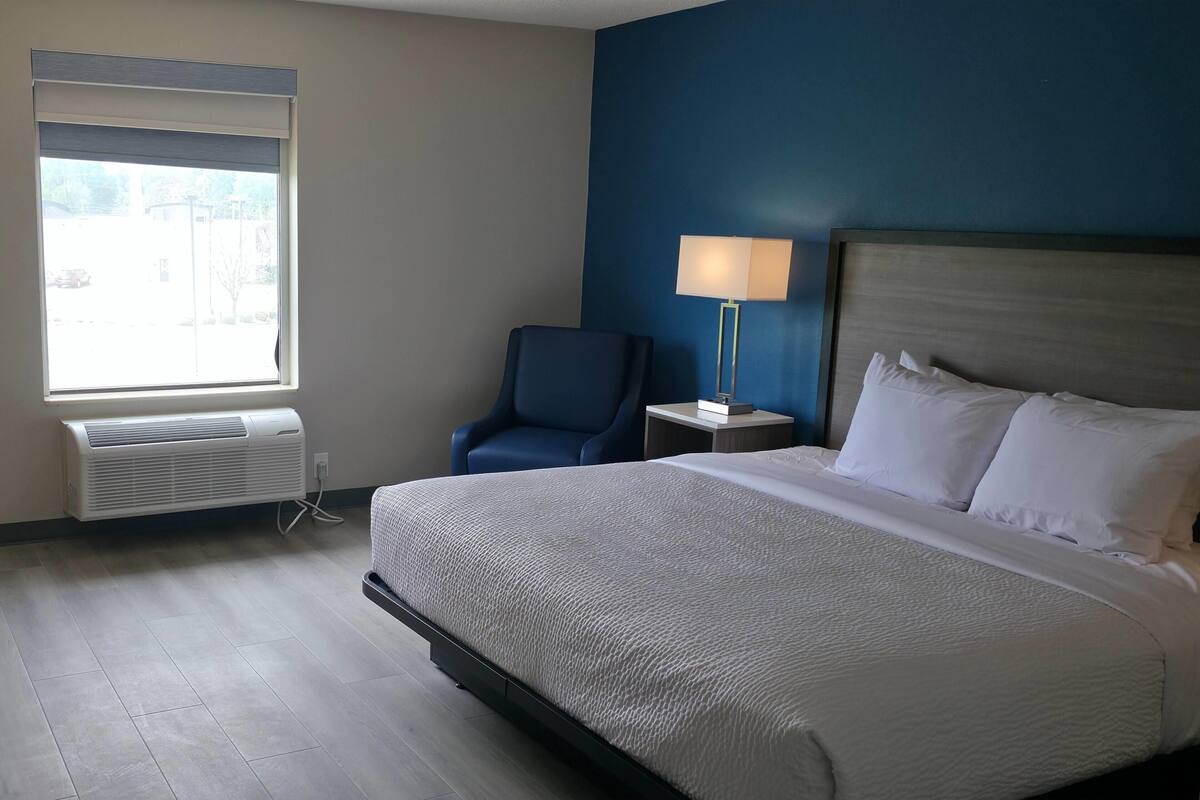 A hotel room with a bed, a chair, a lamp, and a window.