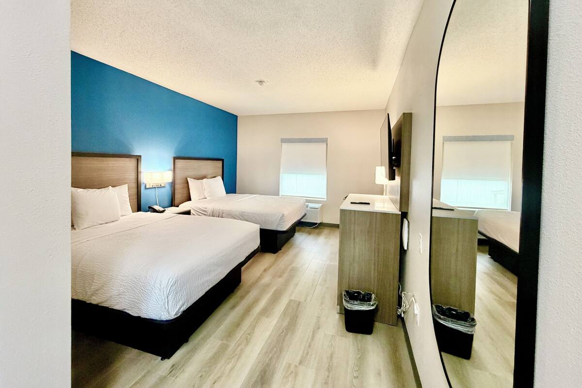 A hotel room with two beds, a desk, a mirror, and a trash bin.