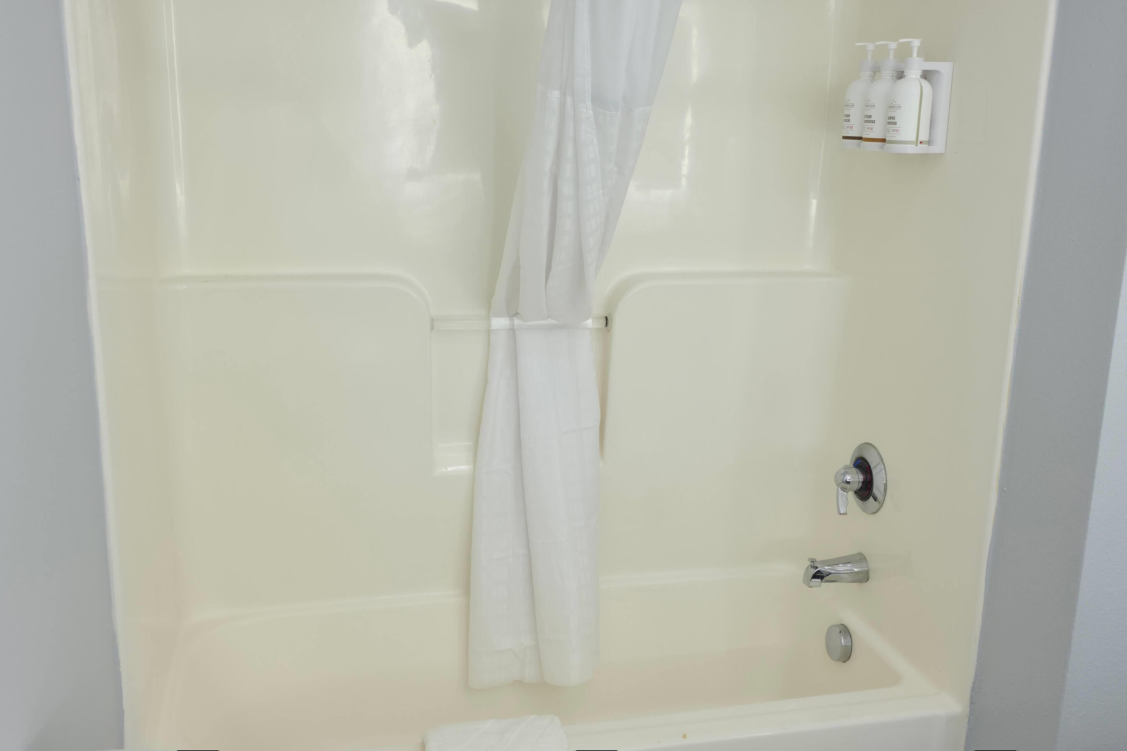 Une baignoire blanche, un rideau de douche, une douchette et un flacon de shampoing fixés au mur.