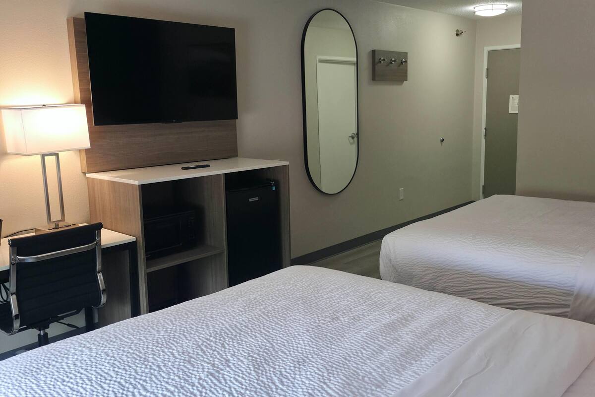 A hotel room with two beds, a TV, a desk with a chair, a mirror, and a lamp.