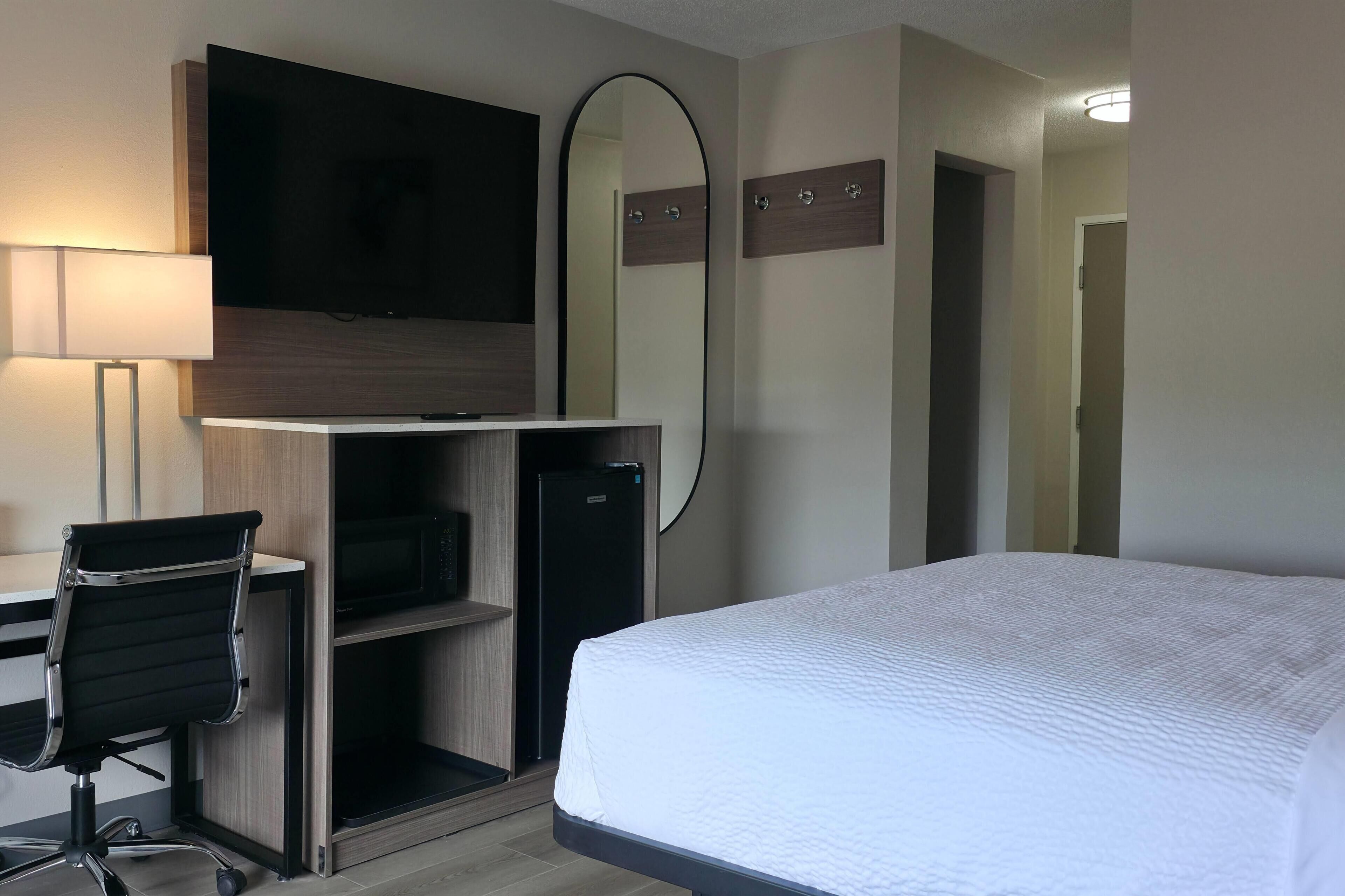 A hotel room with a bed, desk, chair, TV, and a mirror.