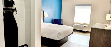 A bedroom with a bed, a desk, a chair, a radiator, and a window.