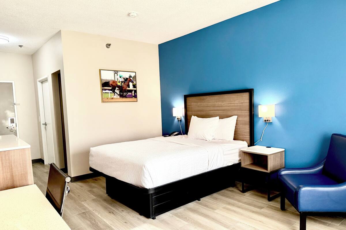 A hotel room with a bed, bedside tables, a chair, a desk, and a wall-mounted picture.