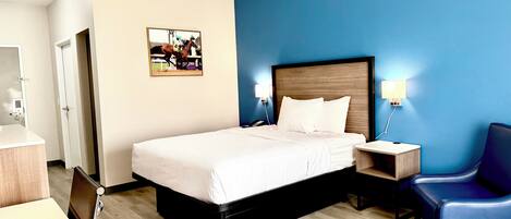 A hotel room with a bed, bedside tables, a chair, a desk, and a wall-mounted picture.