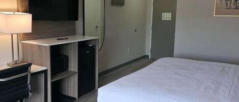 Quarto de hotel com uma cama, uma escrivaninha com luminária, um espelho e uma televisão.
