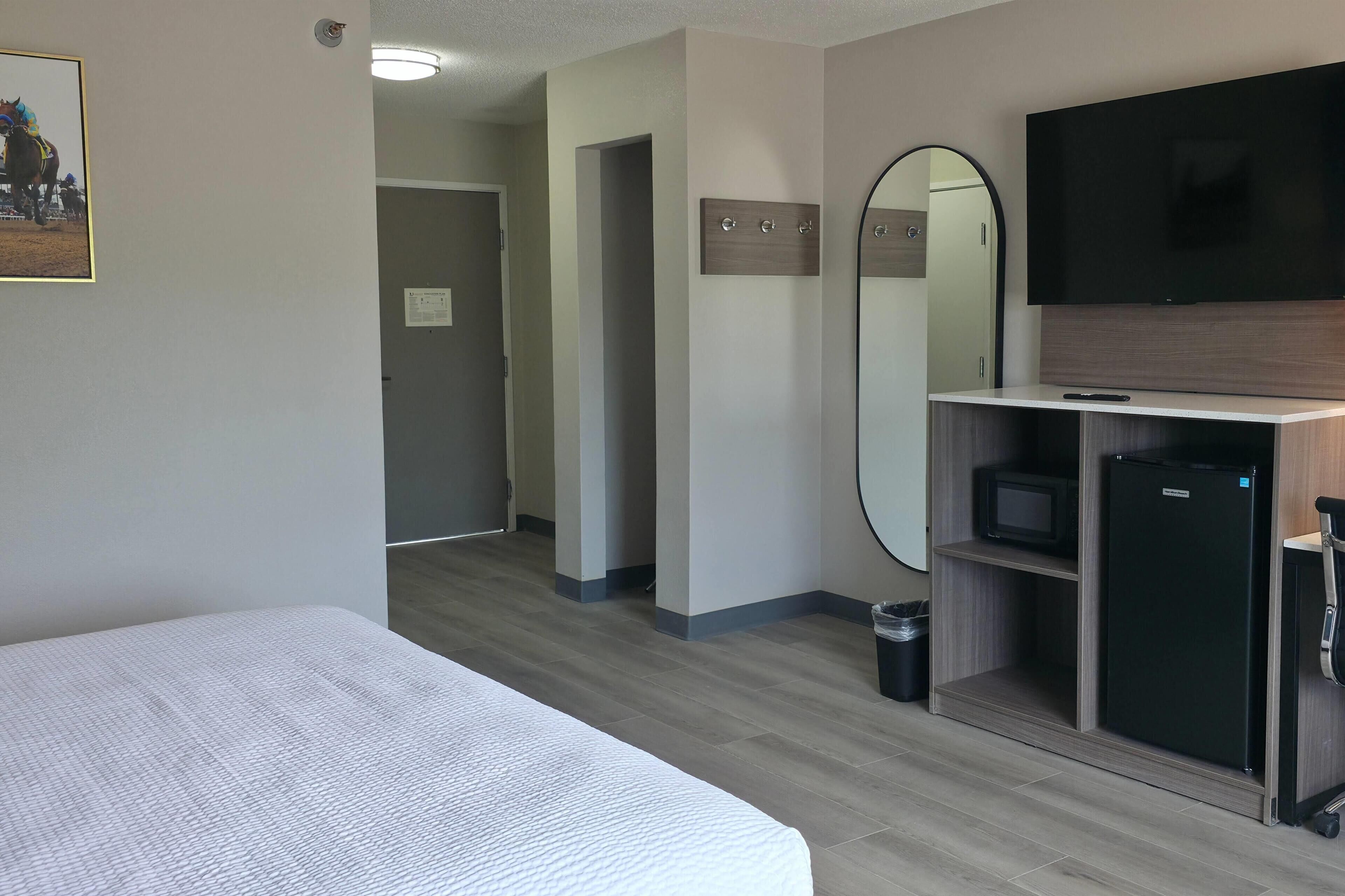 A hotel room with a bed, a TV, a mirror, a small fridge, and a microwave.