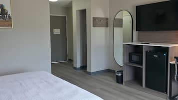 A hotel room with a bed, a TV, a mirror, a small fridge, and a microwave.