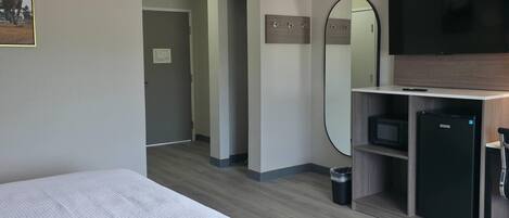 A hotel room with a bed, a TV, a mirror, a small fridge, and a microwave.