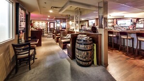 A bar area with wooden furniture, a Guinness barrel, and a counter with a television screen. - Isabella Hotel and Suites (Toronto)