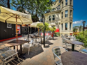 An outdoor patio area with tables and chairs, a sign for a Bloody Refreshment, and a building with stonework and multiple windows.