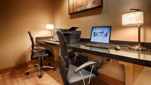 Un bureau d’hôtel équipé d’un bureau, de deux chaises, d’une imprimante, d’un ordinateur portable et d’une lampe.