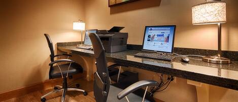 Una oficina de hotel con un escritorio, dos sillas, una impresora, una computadora portátil y una lámpara.