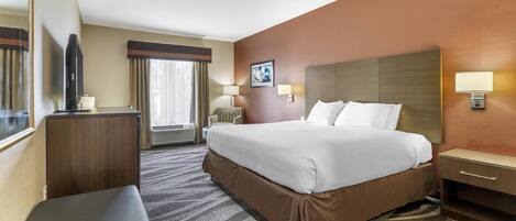 A hotel room with a large bed, a desk, a chair, and a television.