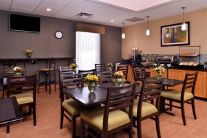 Uma área de refeições de hotel com mesas, cadeiras, um canto de café e um relógio na parede.