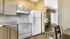 Une cuisine compacte équipée d’une cuisinière, d’un four et d’un réfrigérateur, un coin repas avec une table et des chaises, et un petit espace bureau avec un bureau et une chaise.