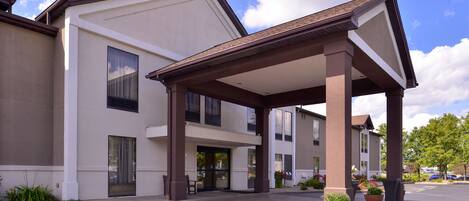 A modern hotel with a covered entrance, large windows, and potted plants.