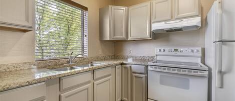 A kitchen with white cabinets, a granite countertop, a built-in oven, and a window with blinds.
