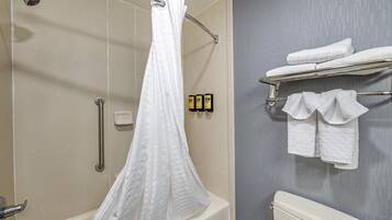 Un baño con ducha, inodoro y un perchero con toallas dobladas.