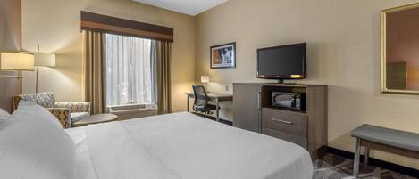 A hotel room with a large bed, a desk with a chair, a television, and a small seating area with a couch and armchairs.