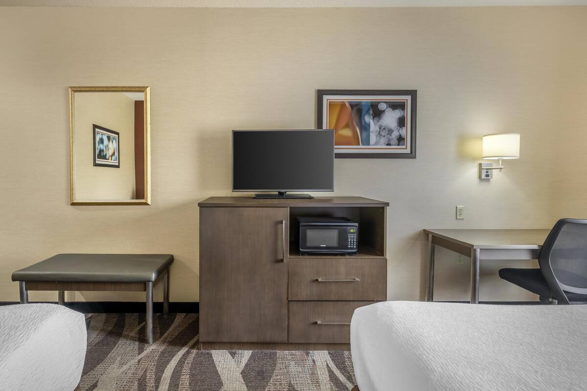 A hotel room with a bed, a desk, a chair, a television, a microwave, and a small table.