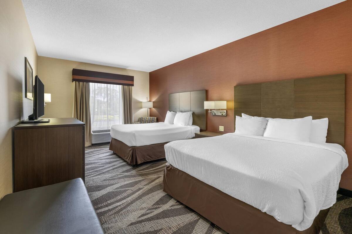 A hotel room with two beds, a desk, a TV, and a large window with curtains.