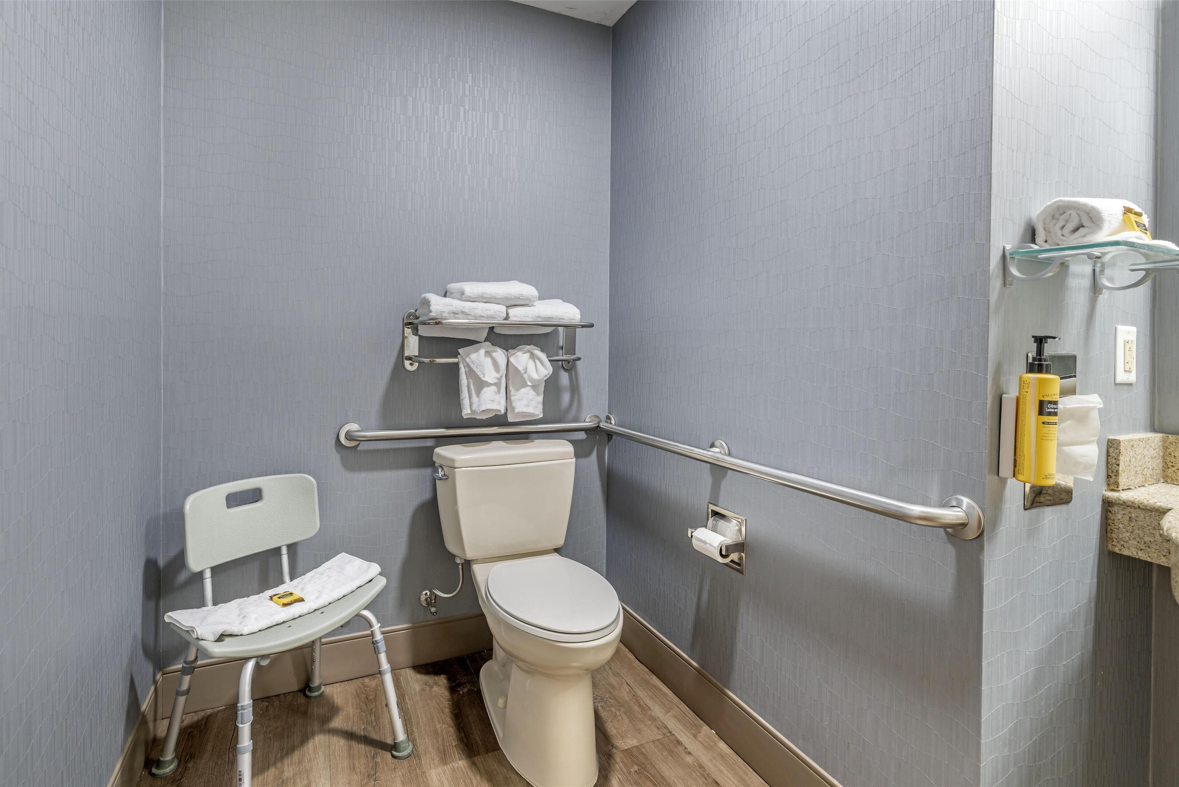Un baño con un inodoro blanco, una silla blanca y una barra de apoyo.