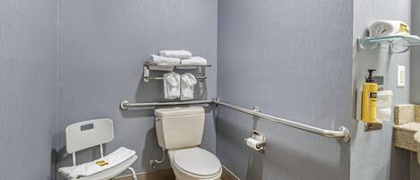 Un baño con un inodoro blanco, una silla blanca y una barra de apoyo.