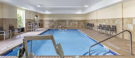 A swimming pool with a lifeguard chair, a changing room, and a seating area with chairs.