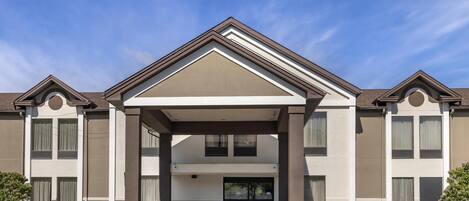 A hotel with a modern facade, a covered entrance, and a landscaped front yard.