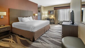 Une chambre d’hôtel avec un grand lit, un bureau avec une chaise, une télévision et une fenêtre avec des rideaux.