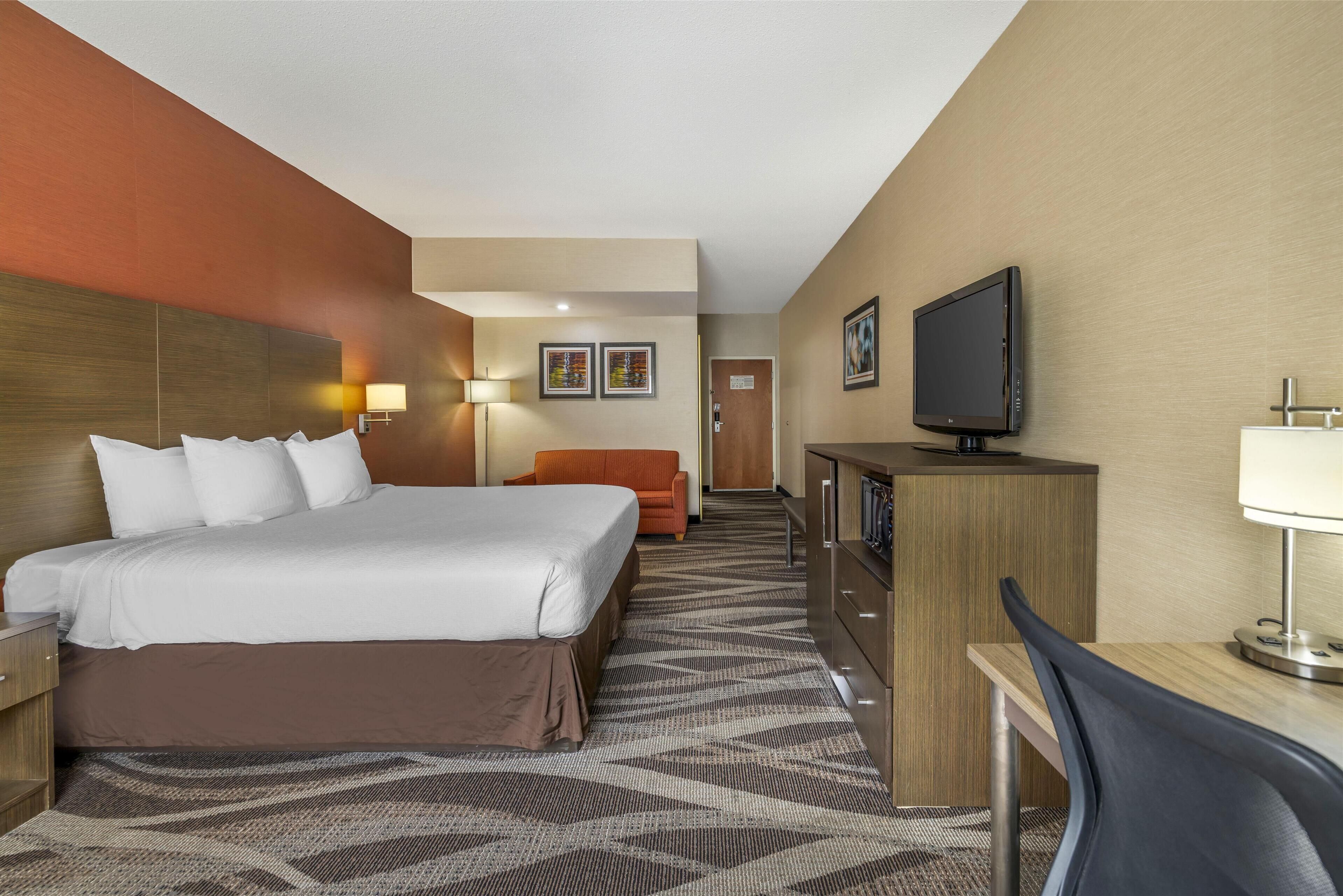 A hotel room with a large bed, a desk with a chair, a television, and a desk lamp.